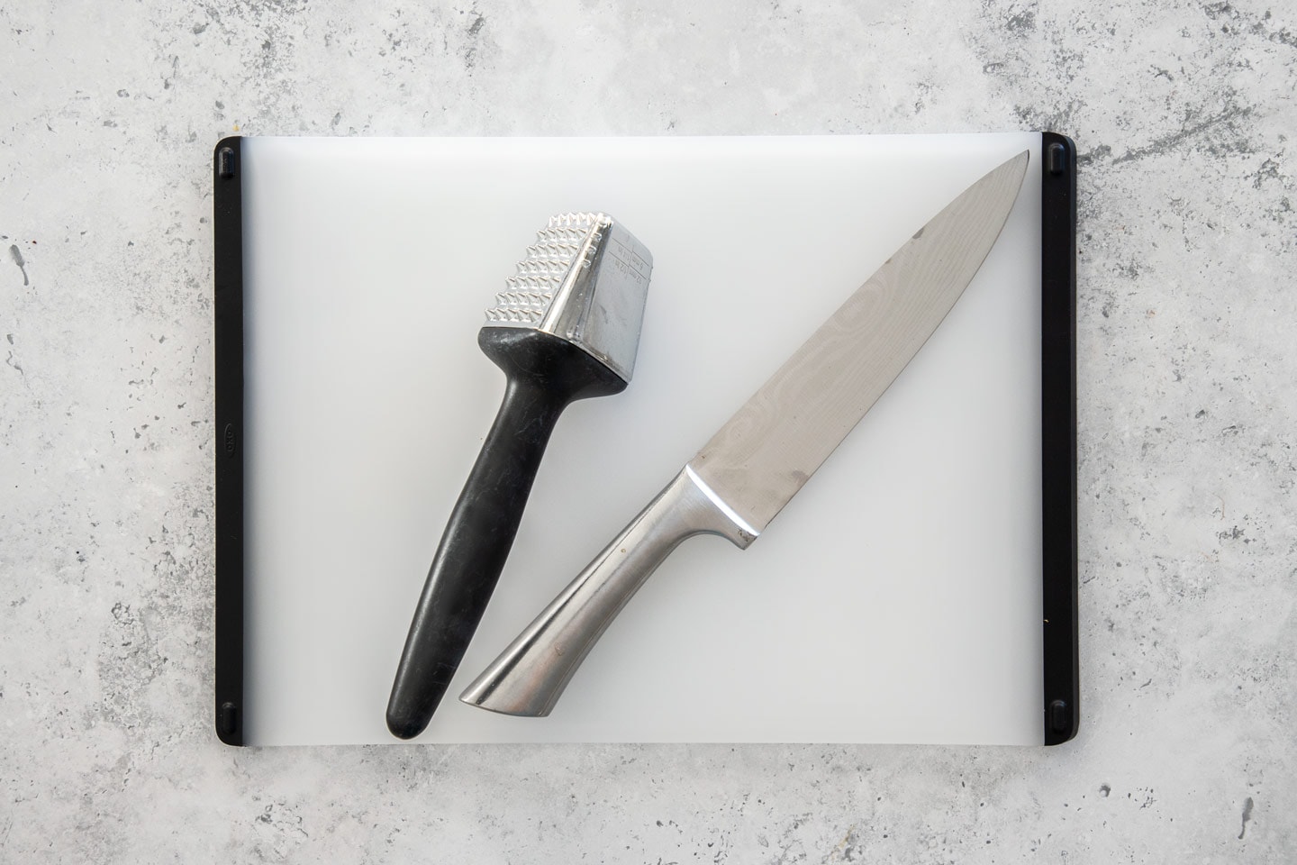 A chefs knife, meat tenderiser and chopping board.
