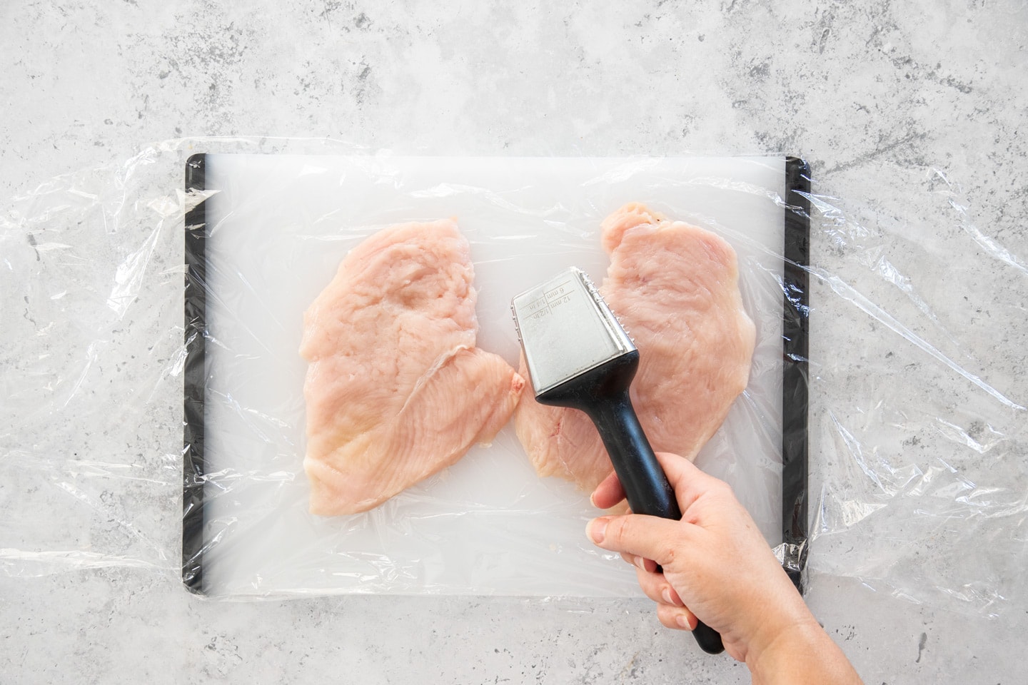 Two chicken cutlets on a chopping board that have been pounded.