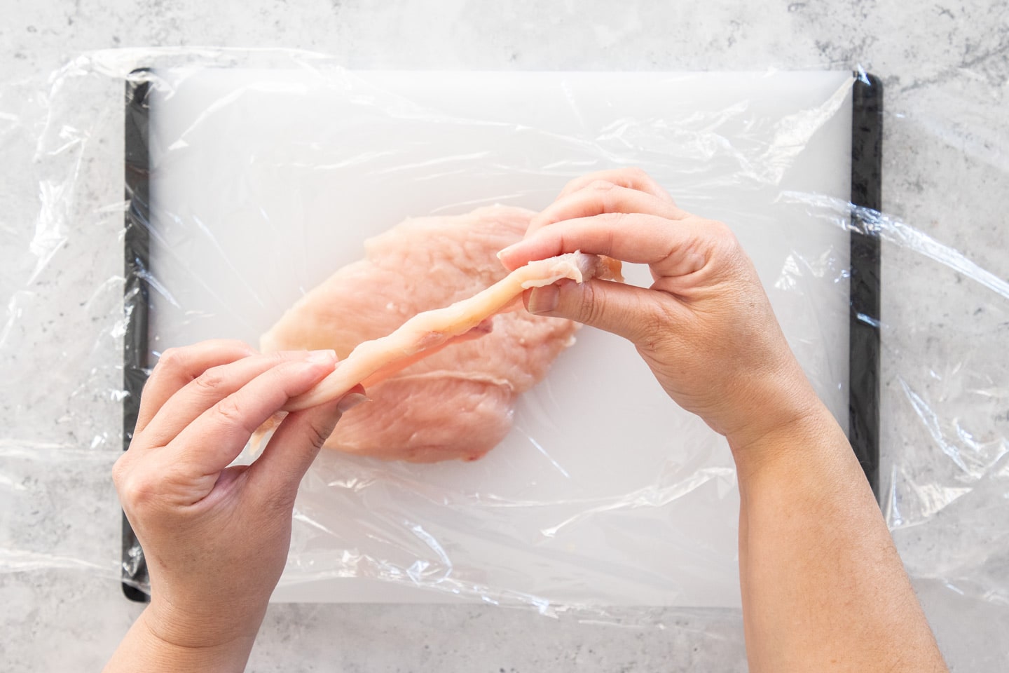Hands holding a chicken cutlet to show the thickness.