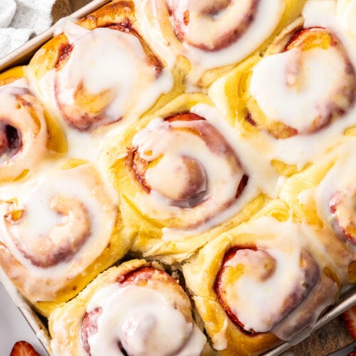 A batch of strawberry cinnamon rolls with white icing.