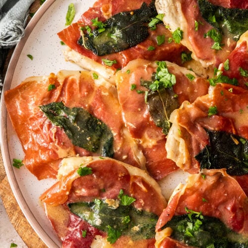 Slices of cooked prosciutto topped chicken on a plate.
