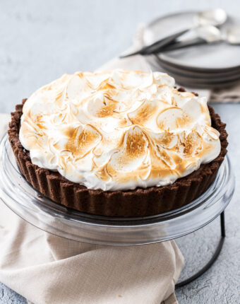 A whole chocolate meringue pie on a cake platter.