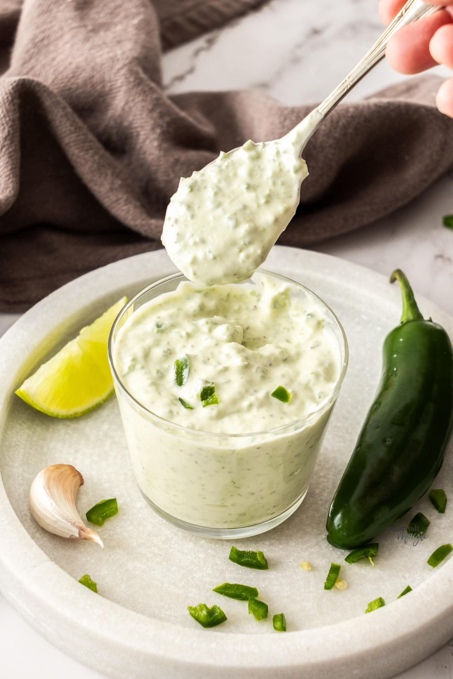 A spoon taking jalapeno mayo out of a glass.