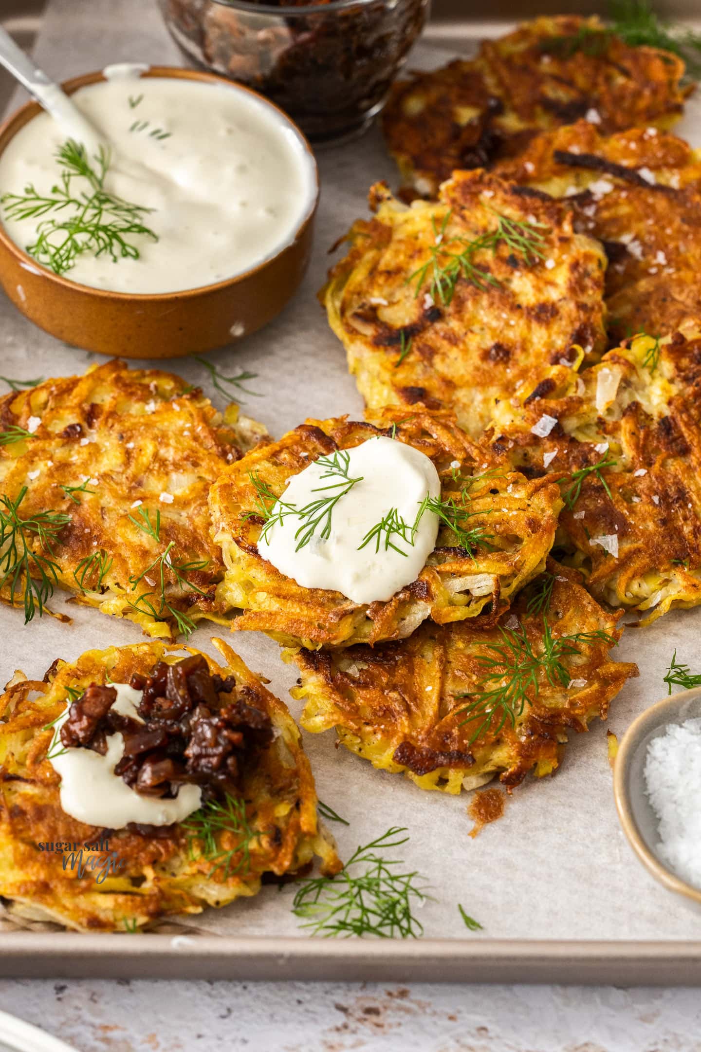 Potato fritters on a baking tray, one topped with sour cream.