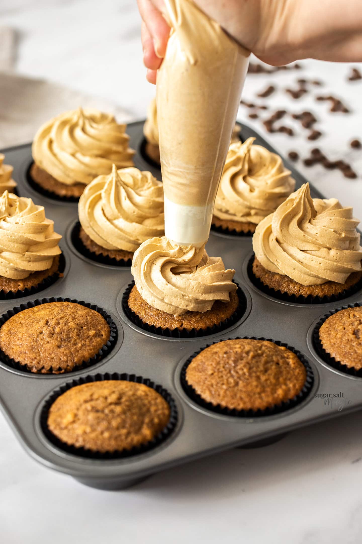 Coffee buttercream being piped onto a cupcake.