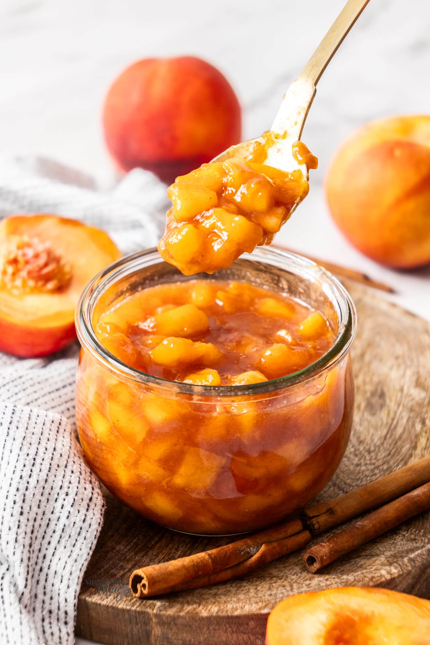 A spoon taking peach compote from a jar.