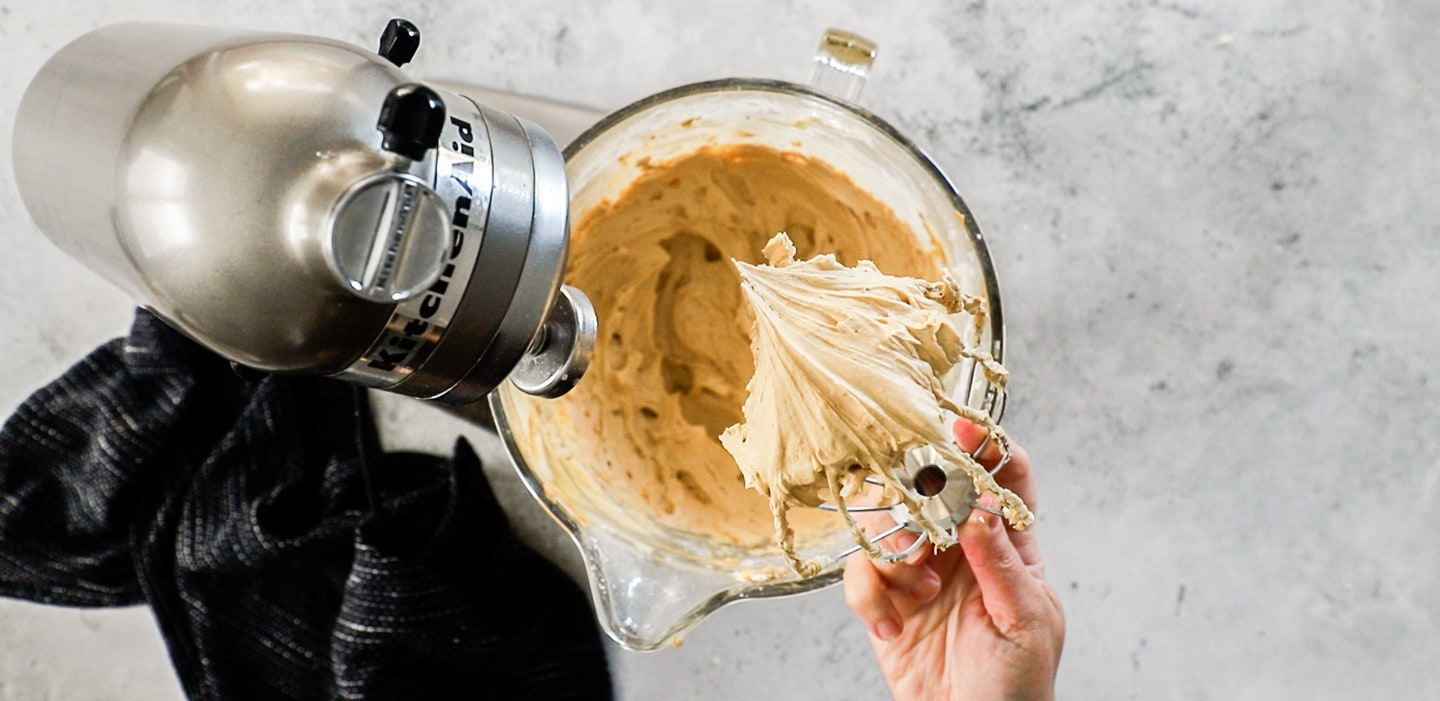 A hand holding a whisk with coffee buttercream.