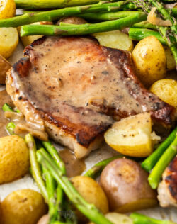A pork chop with potatoes and asparagus with sauce on top.