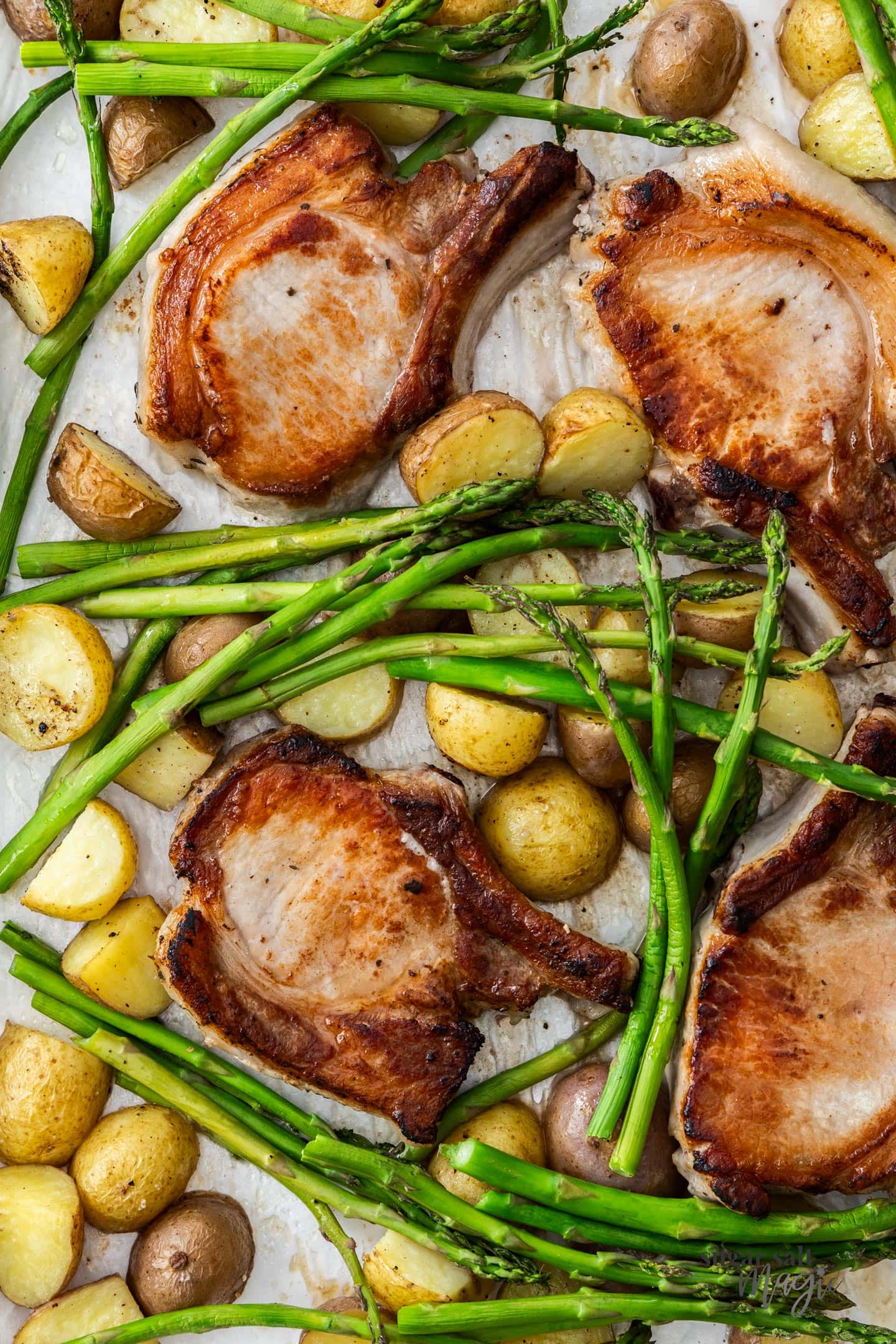 4 pork chops with potatoes and asparagus on a baking tray.