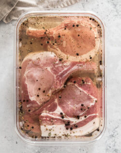 Pork chops in brine in a glass dish.