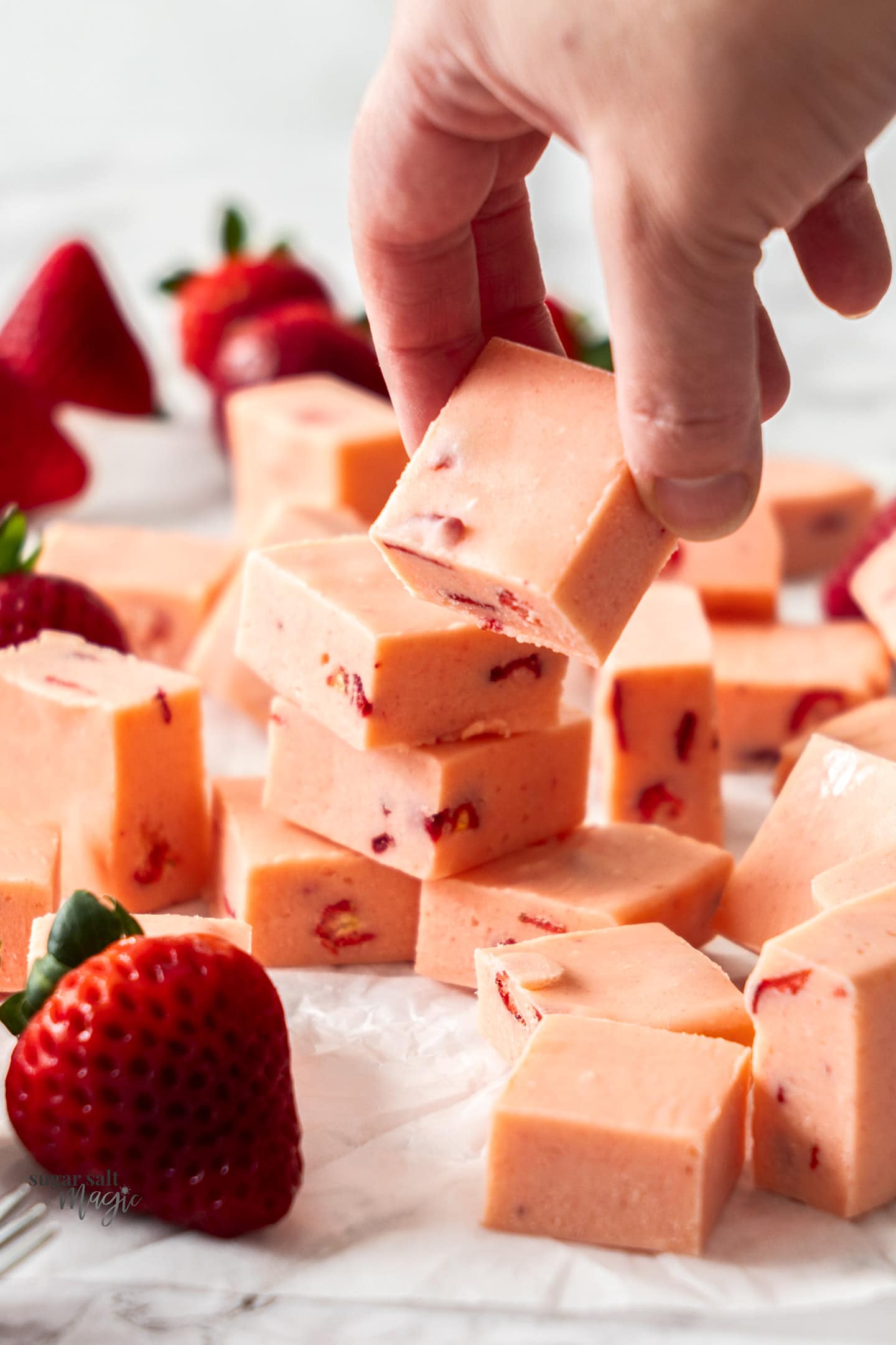 A hand picking up a piece of strawberry fudge.