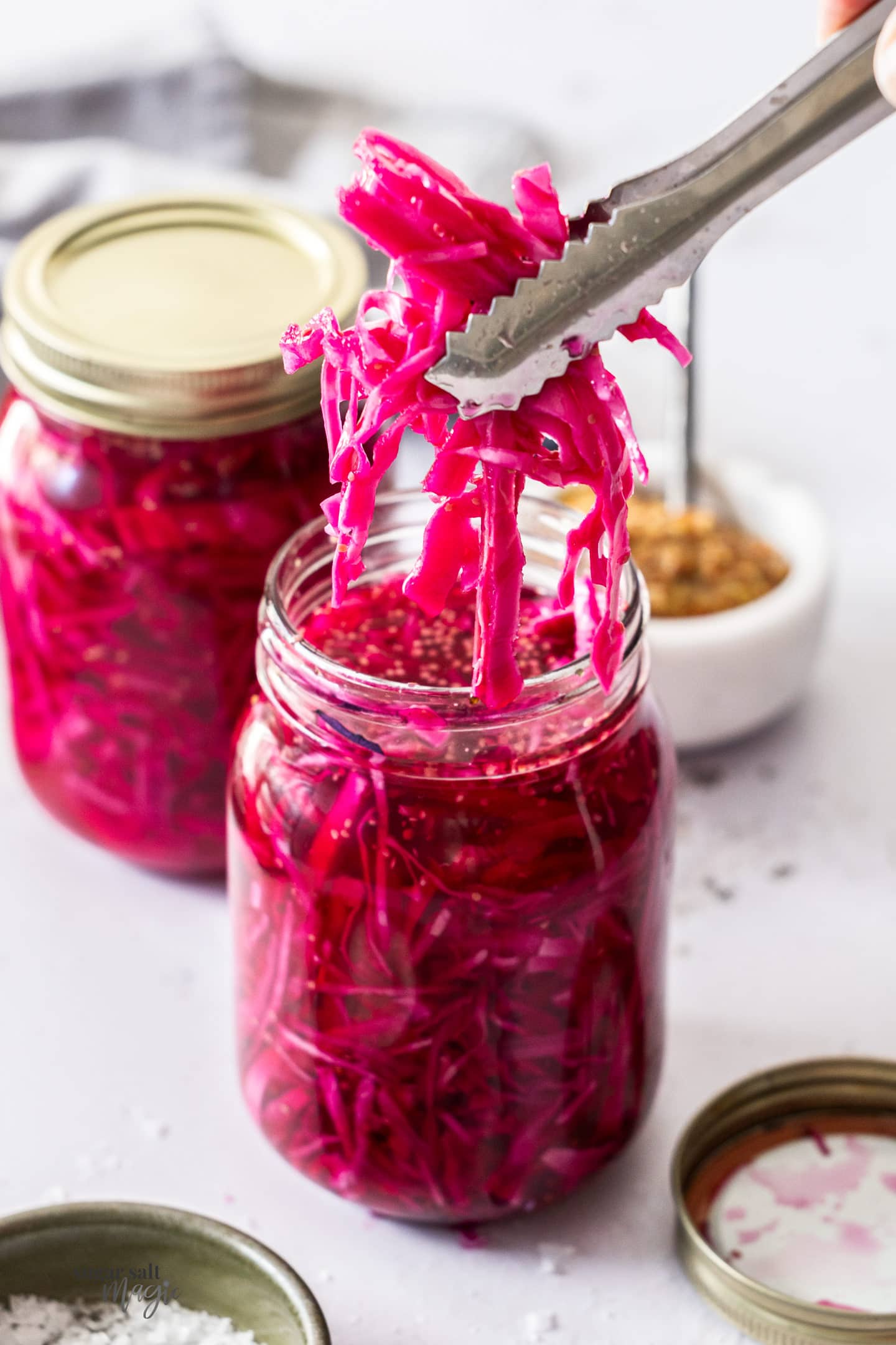 Tongs taking pickled red cabbage out of a jar.