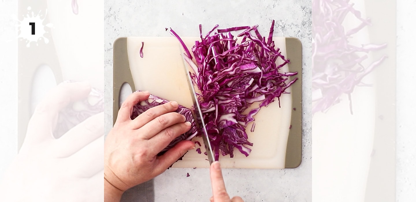Finely slicing red cabbage on a chopping board.