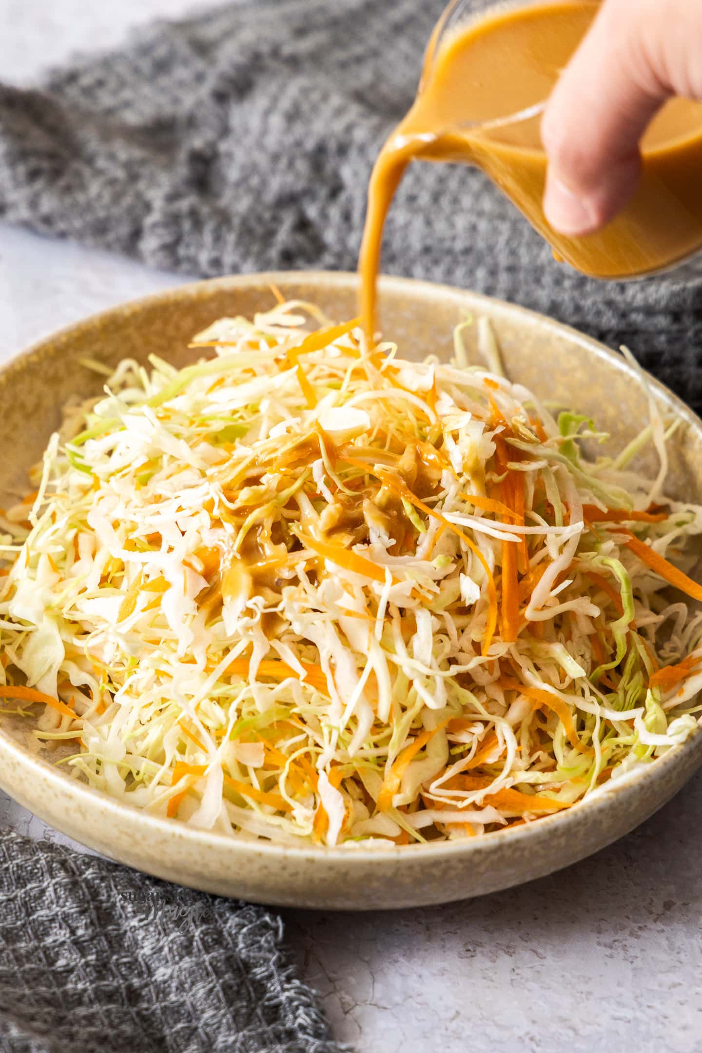 Japanese sesame dressing being poured over shredded cabbage and carrot.