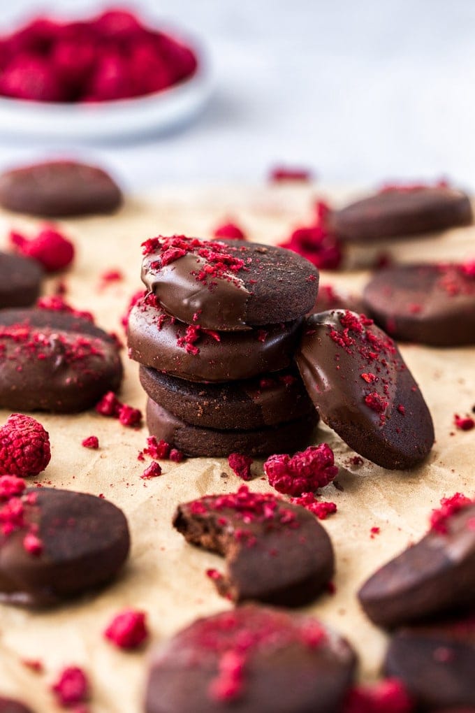 closeup: a stack of chocolate shortbread cookies recipe sprinkled with freeze-dried raspberries on a sheet of brown baking paper