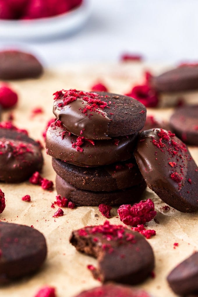 a stack of dark chocolate shortbread cookies, sprinkled with freeze-dried raspberries on a sheet of brown parchment paper