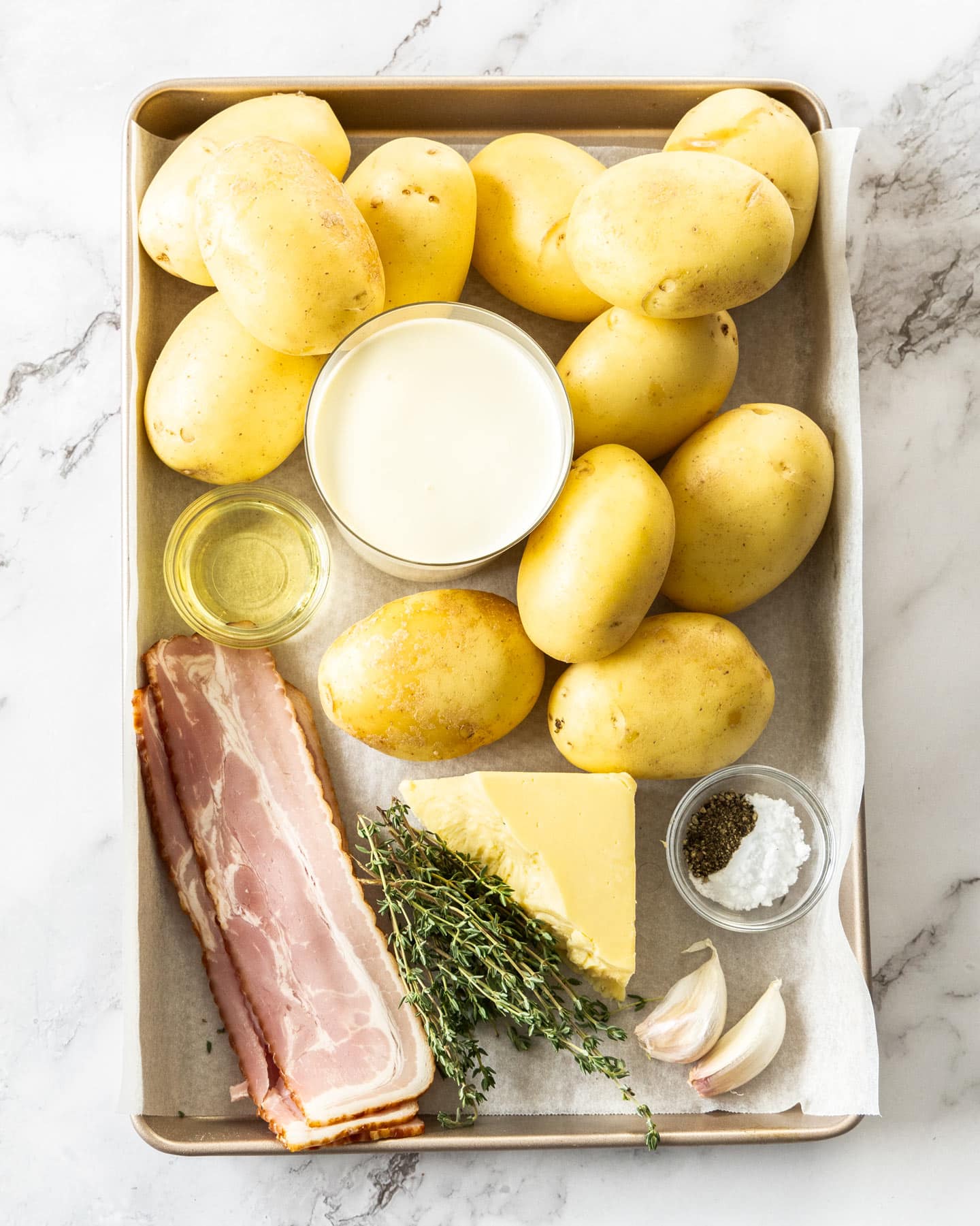 Ingredients for hasselback potato gratin on a baking tray.