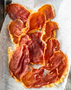 Pieces of flat crisp prosciutto on a metal tray.