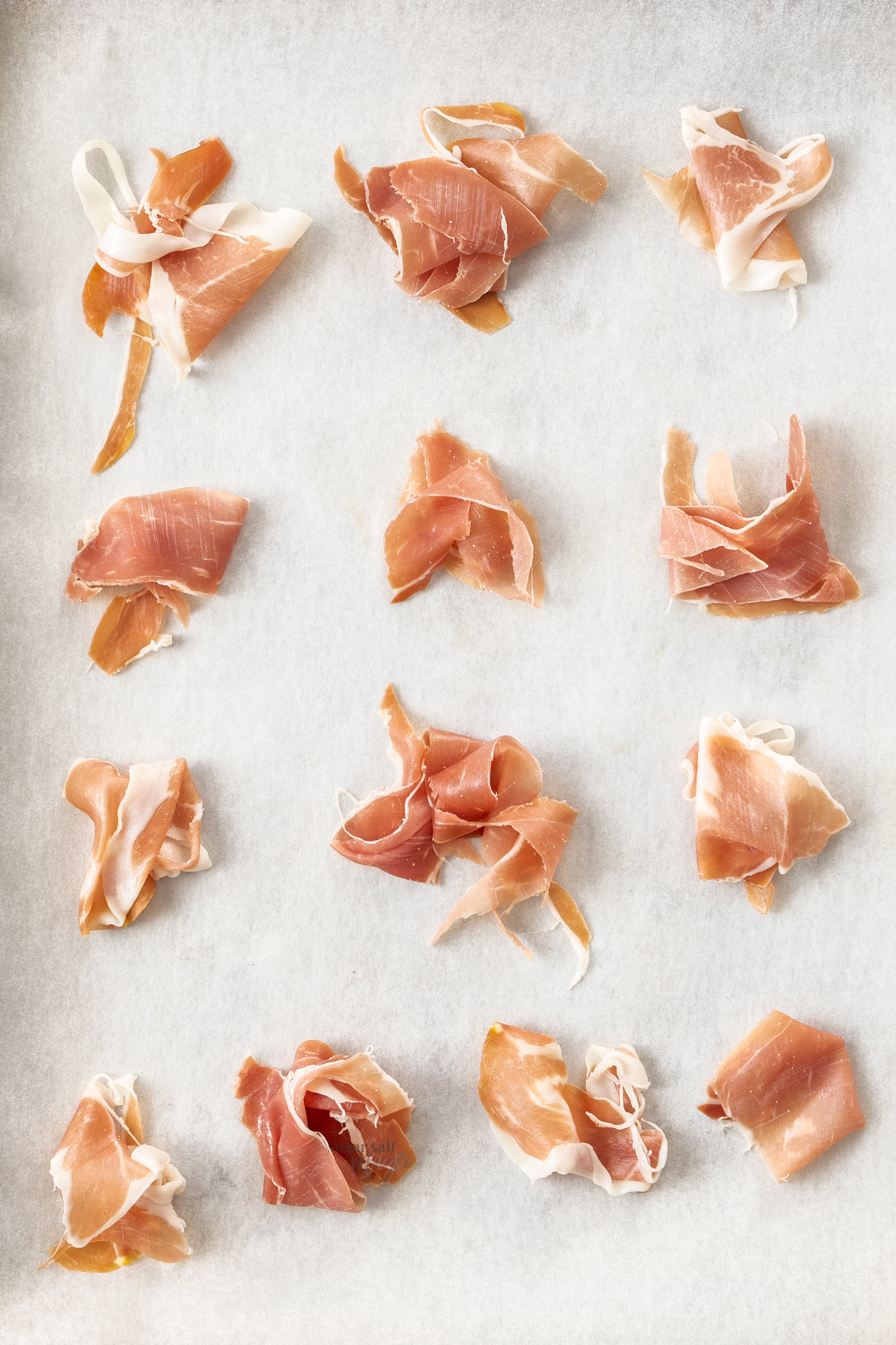 Small piles of prosciutto on a baking tray ready to bake.