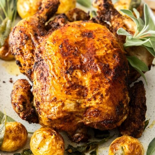 Whole air fryer roast chicken with sage potatoes in a serving platter.