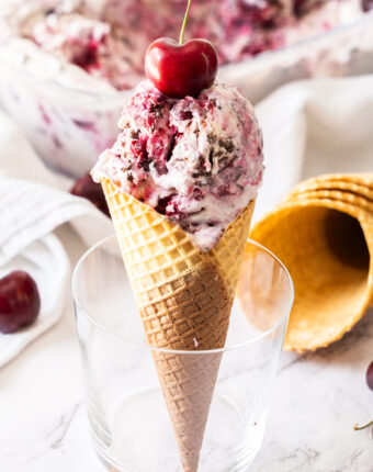 A waffle cone with scoops of black forest ice cream standing in a glass.