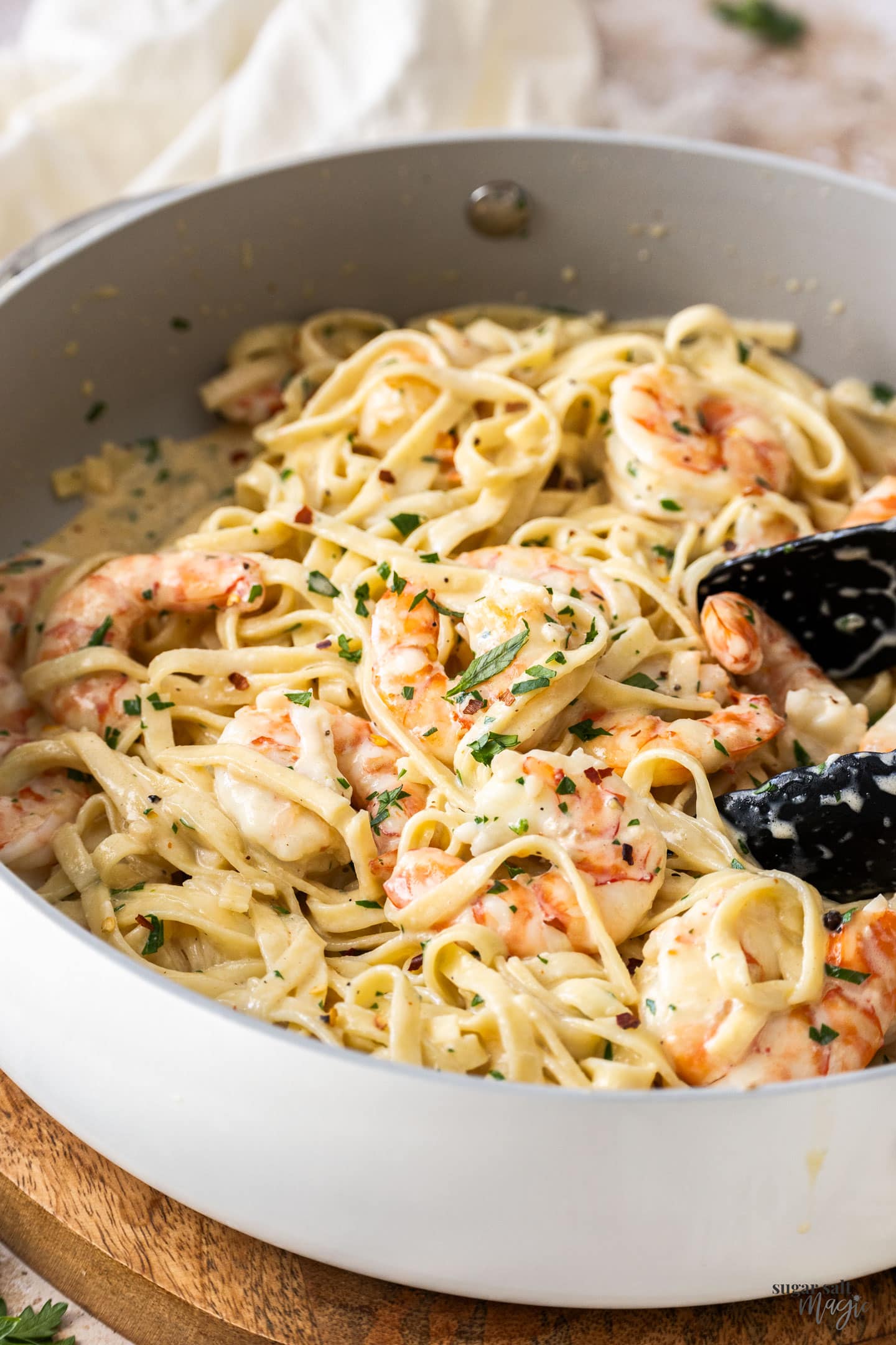 Prawns and creamy linguine in a pan with tongs on the side.