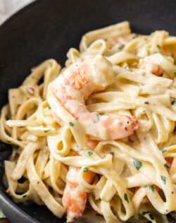 Super close up of a creamy prawn sitting on top of linguine.