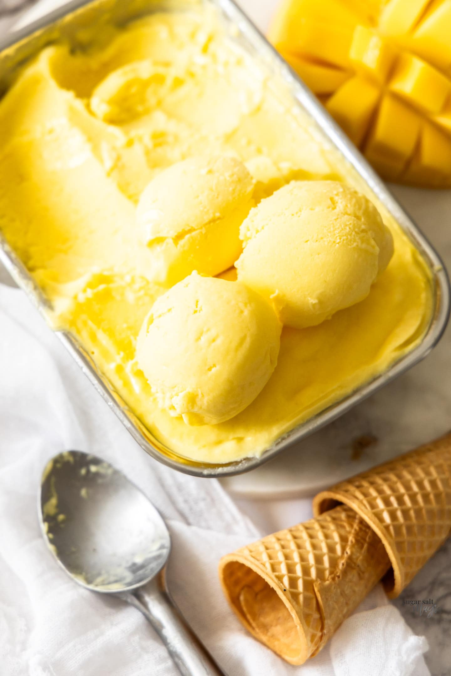 Scoops of mango gelato on top of the pan full of it.