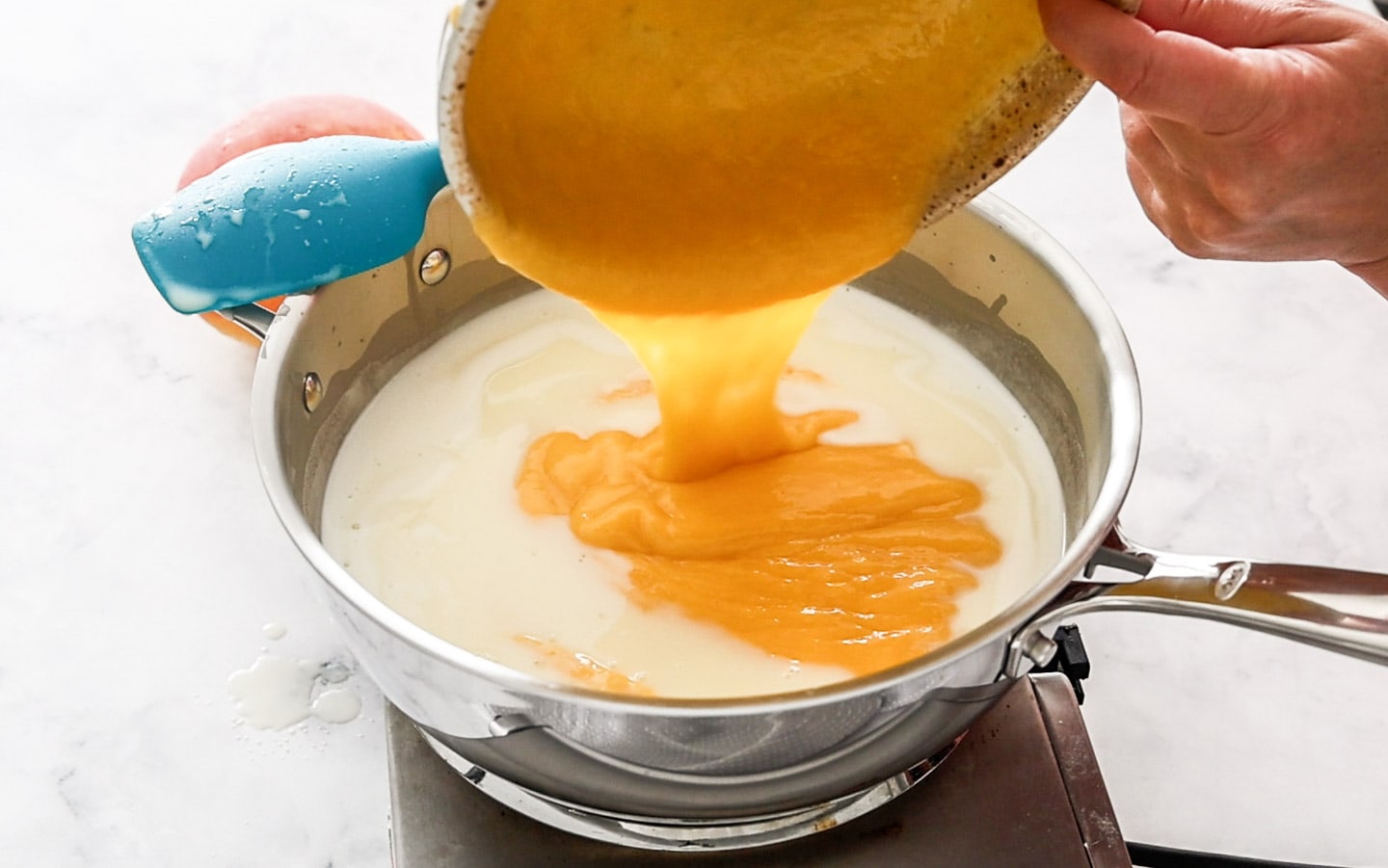 Adding mango puree to hot milk in a saucepan.