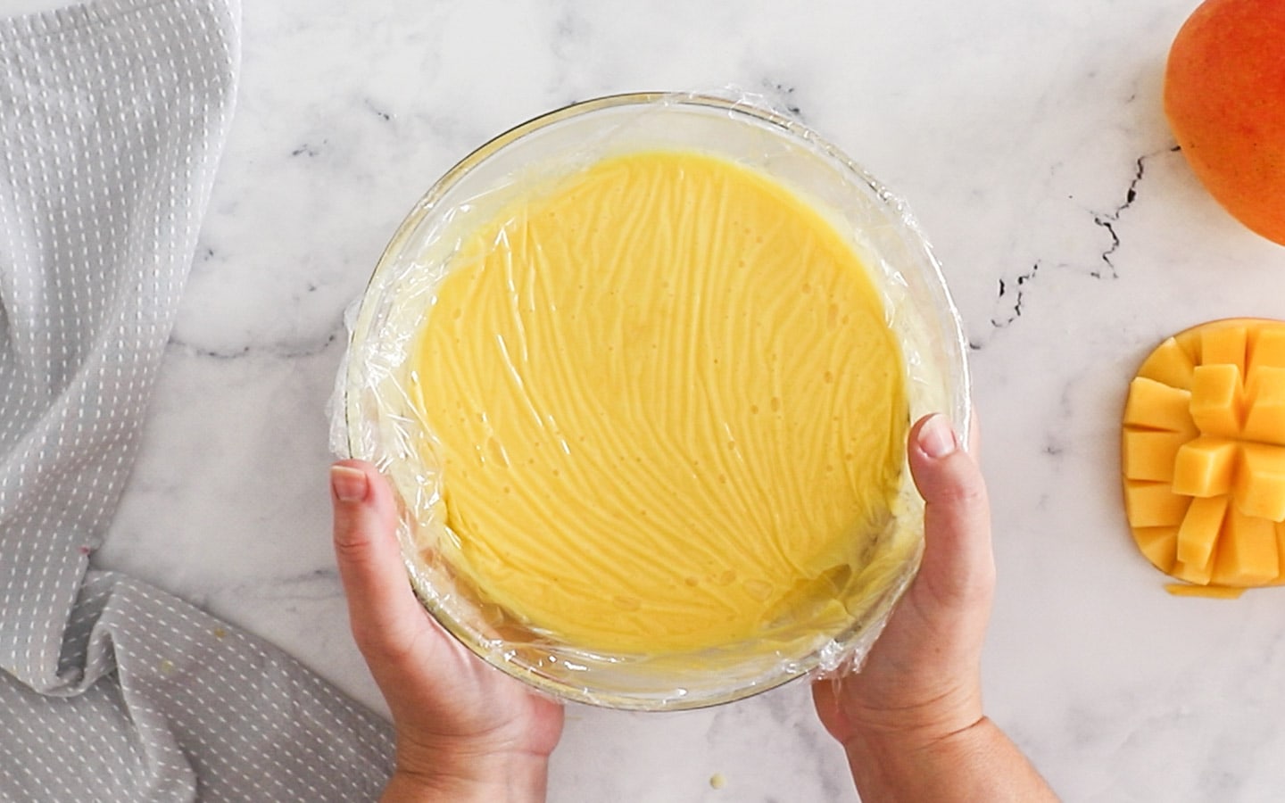 A bowl of mango custard with plastic wrap pressed to the surface.
