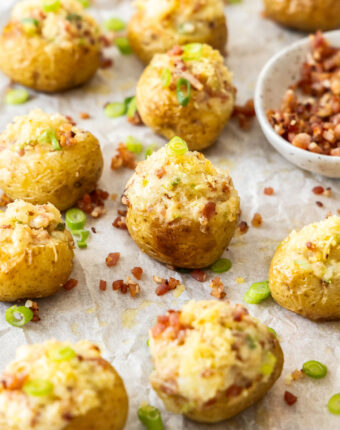 A whole batch of mini baked potatoes with bits of bacon scattered around.