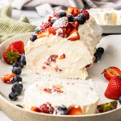 A pavlova roll topped with berries with one slice cut away.