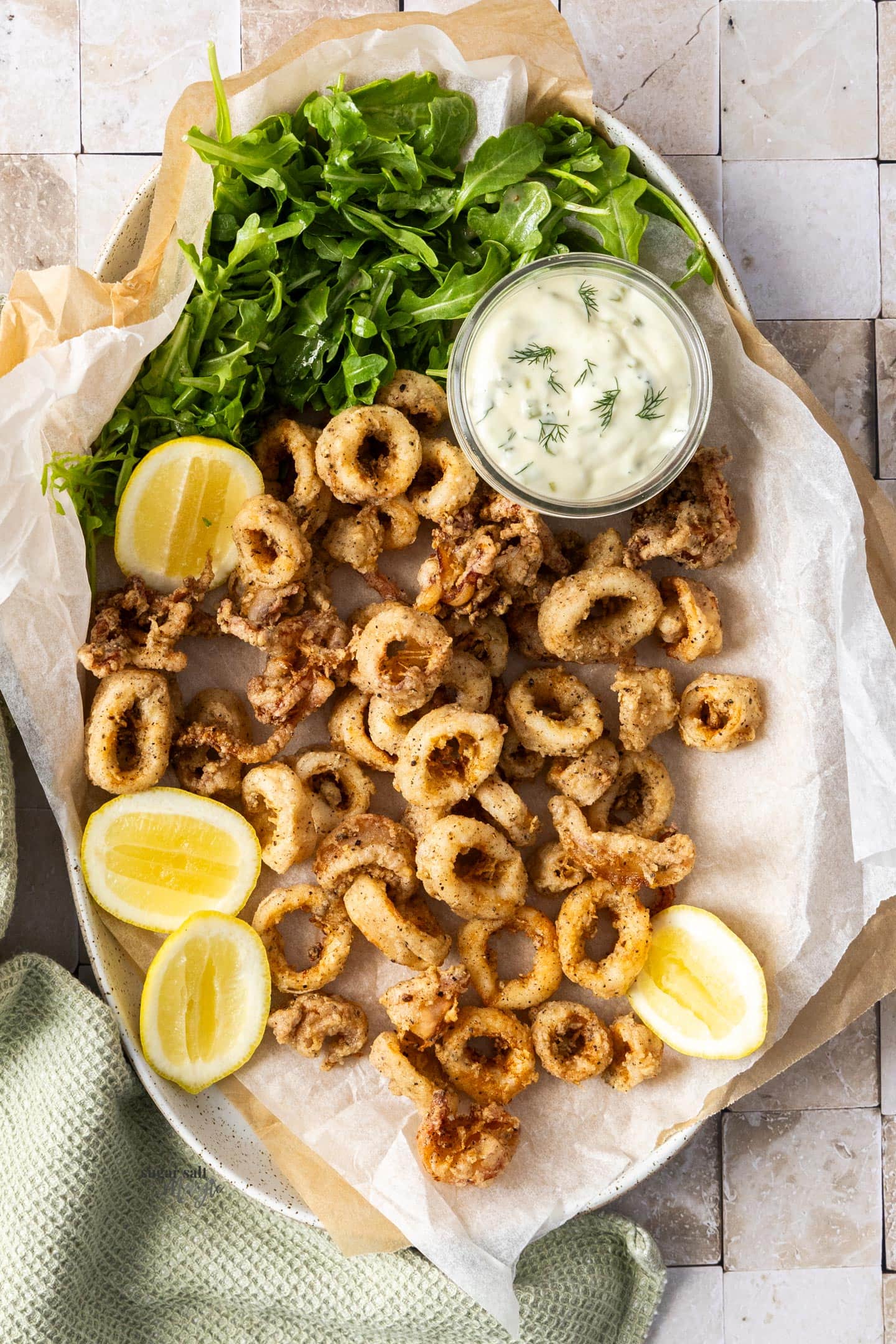 Top down view of salt and pepper calamari with lemons and mayonnaise.