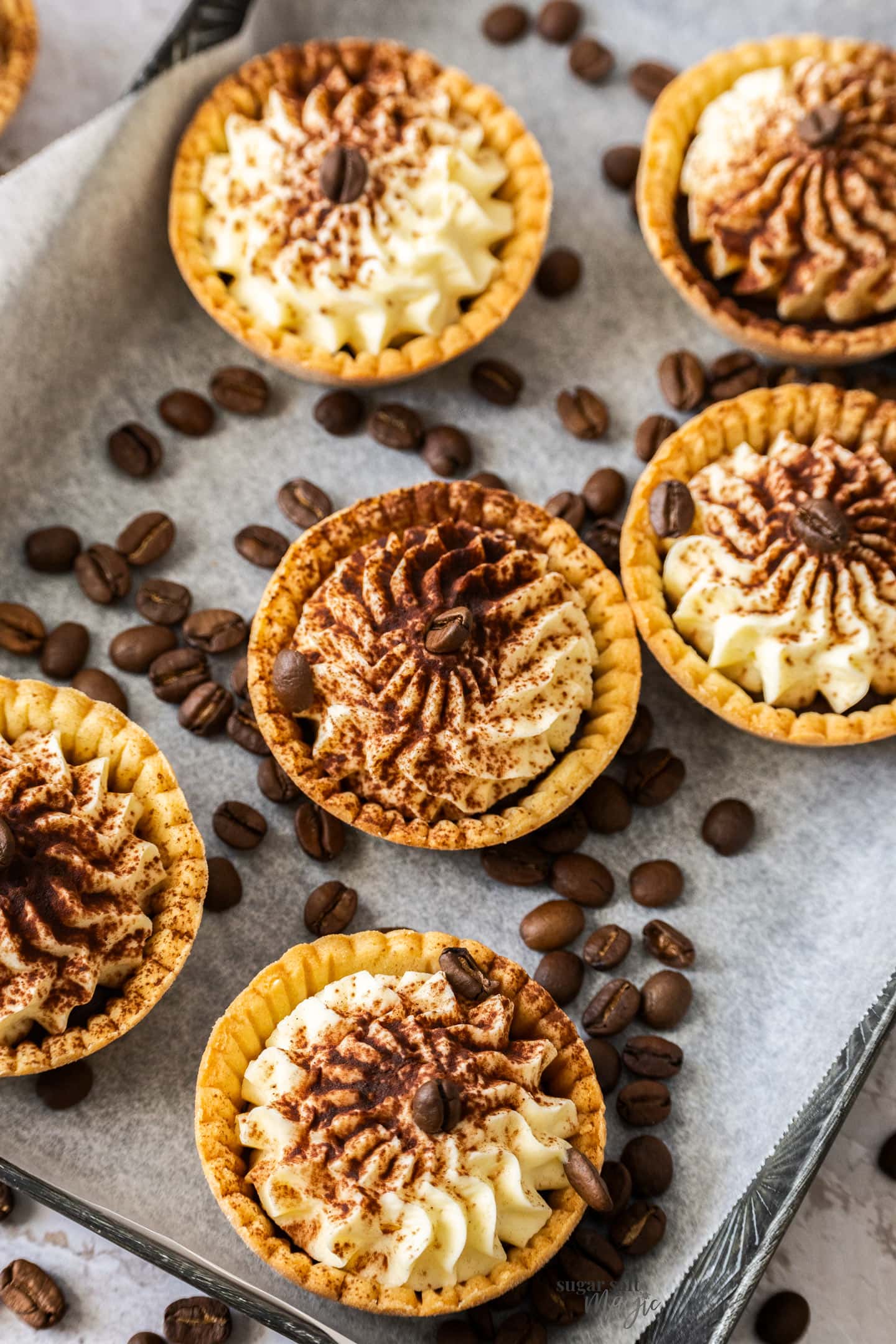 6 cream filled tartlets on a metal tray surrounded by coffee beans.