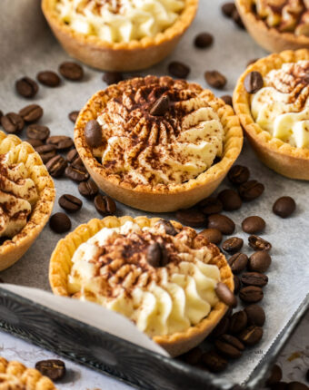 A batch of tartlets on a metal tray, surrounded by coffee beans.