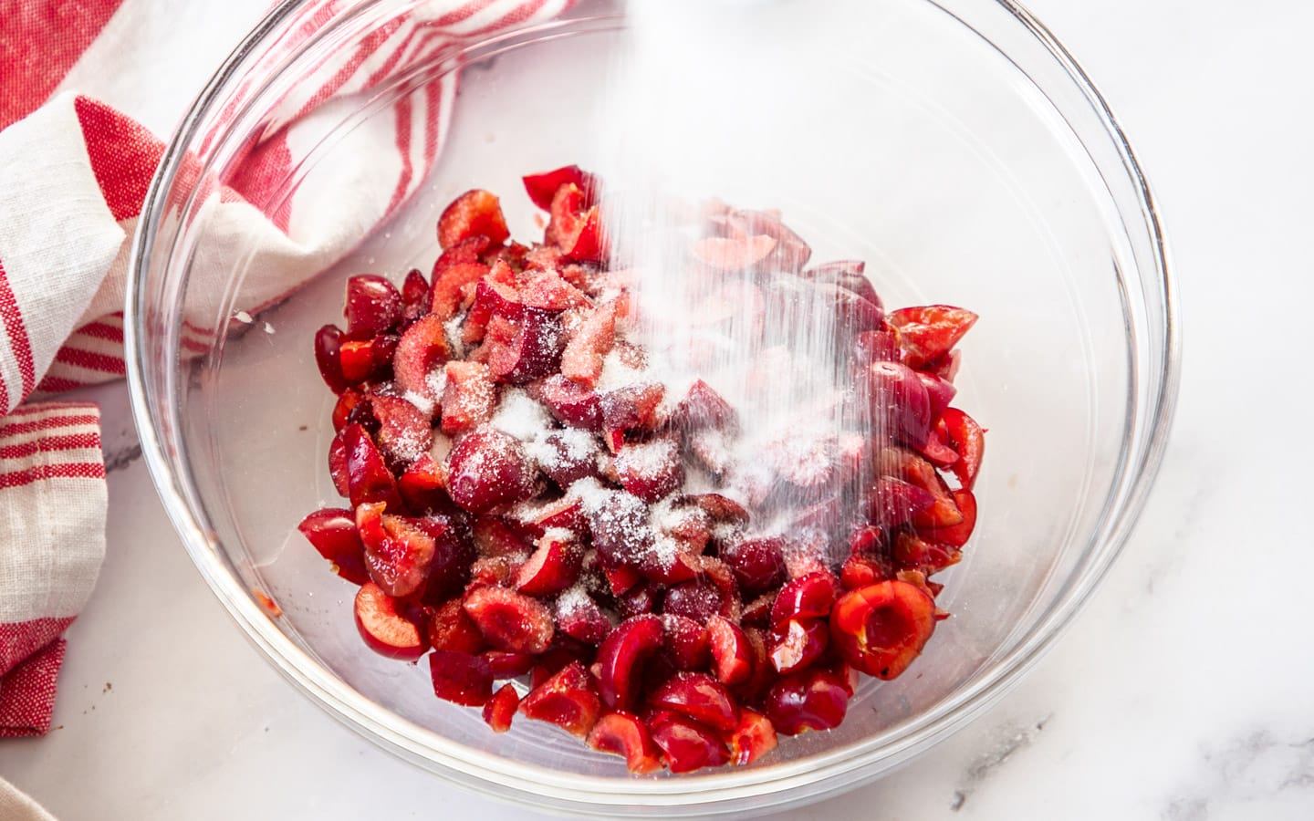 Sugar being poured over fresh cherries in a bowl.