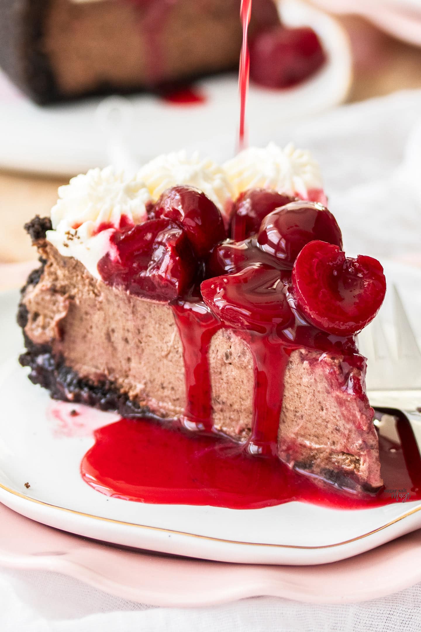 A slice of black forest cheesecake with sauce being poured over.