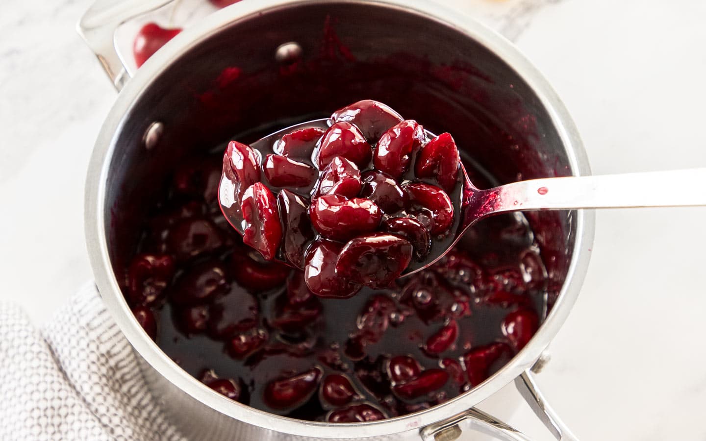 A scoop of cherry sauce being taken from a saucepan.