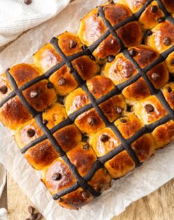 A batch of freshly baked hot cross buns on a wooden board.