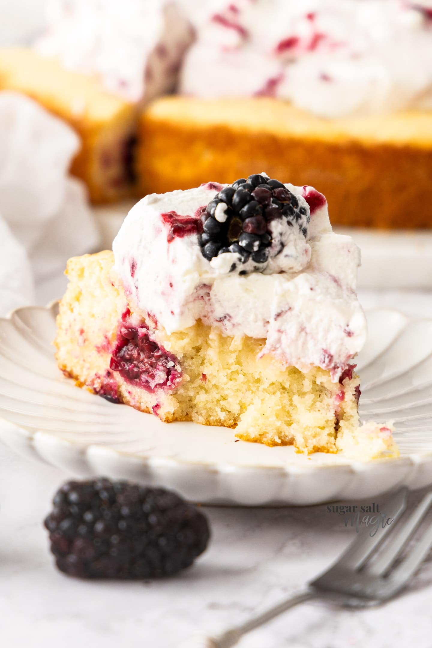 A slice of lemon blackberry cake with a forkful removed.