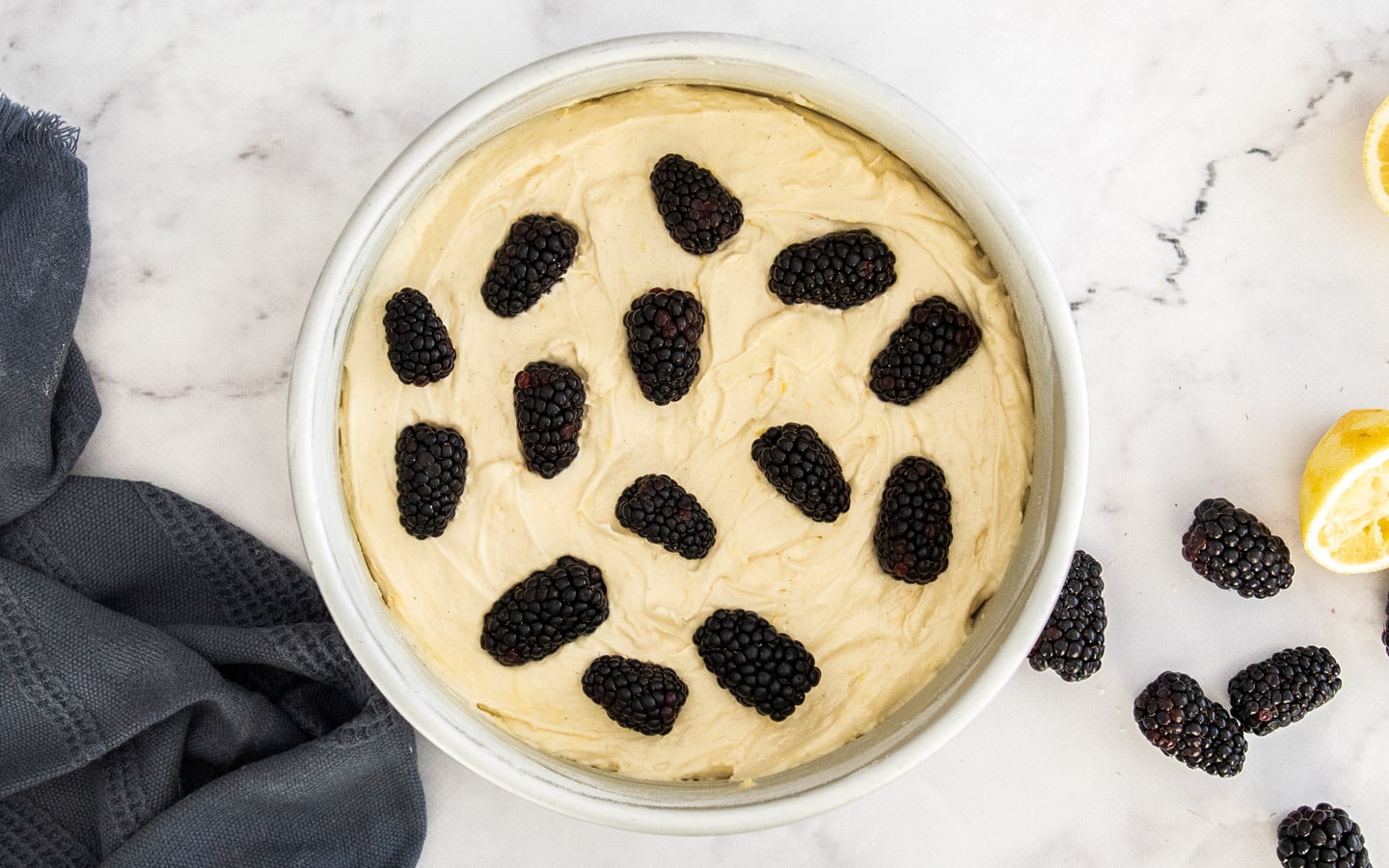 The batter in a cake pan dotted with blackberries.