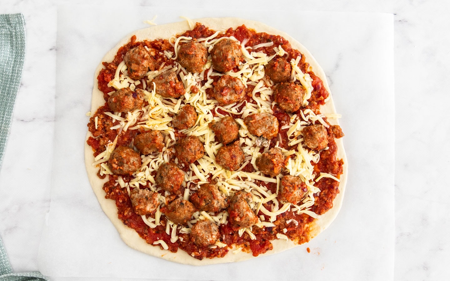 The pizza base topped with sauce, cheese and meatballs.