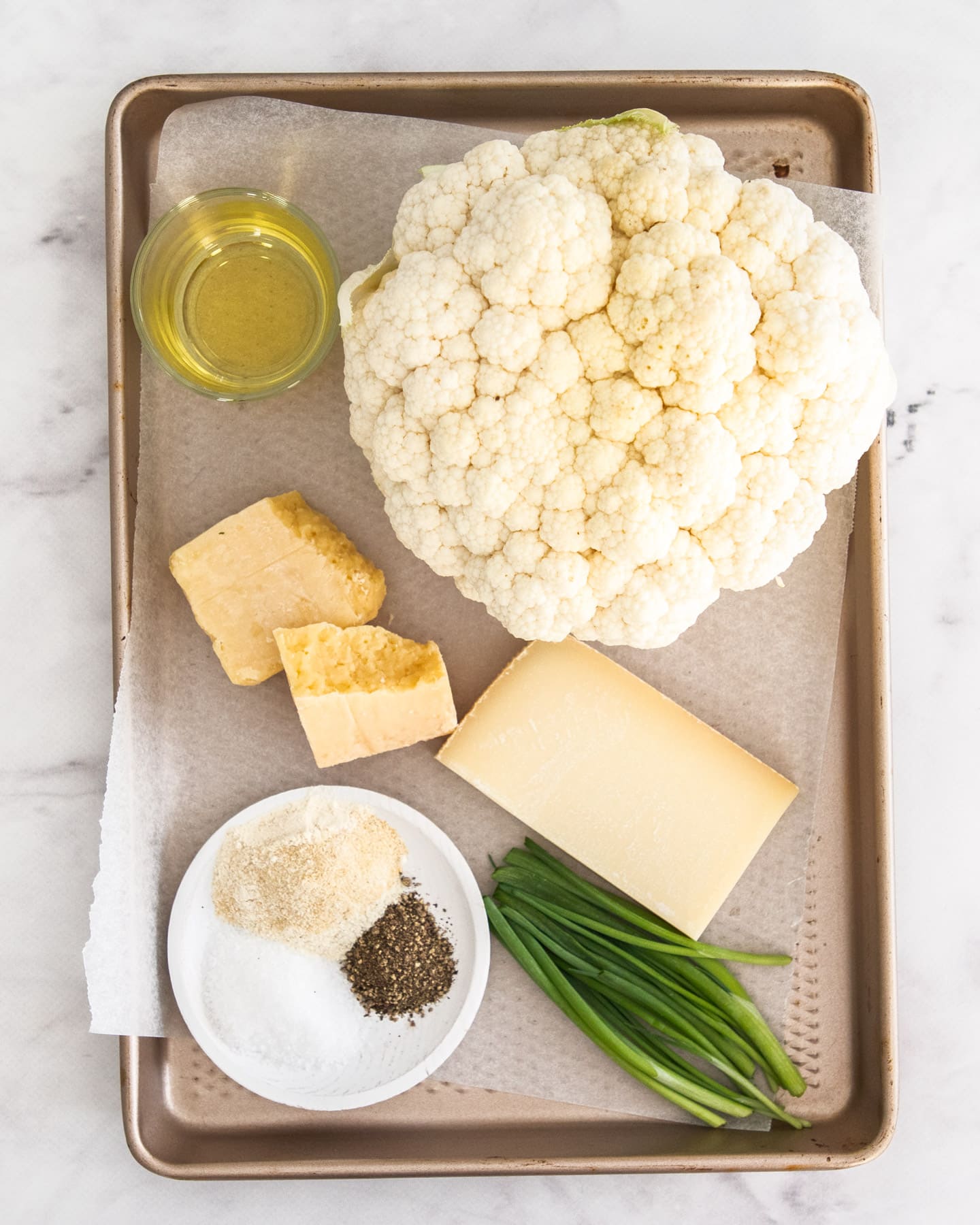Ingredients for cheesy cauliflower steaks on a baking tray.