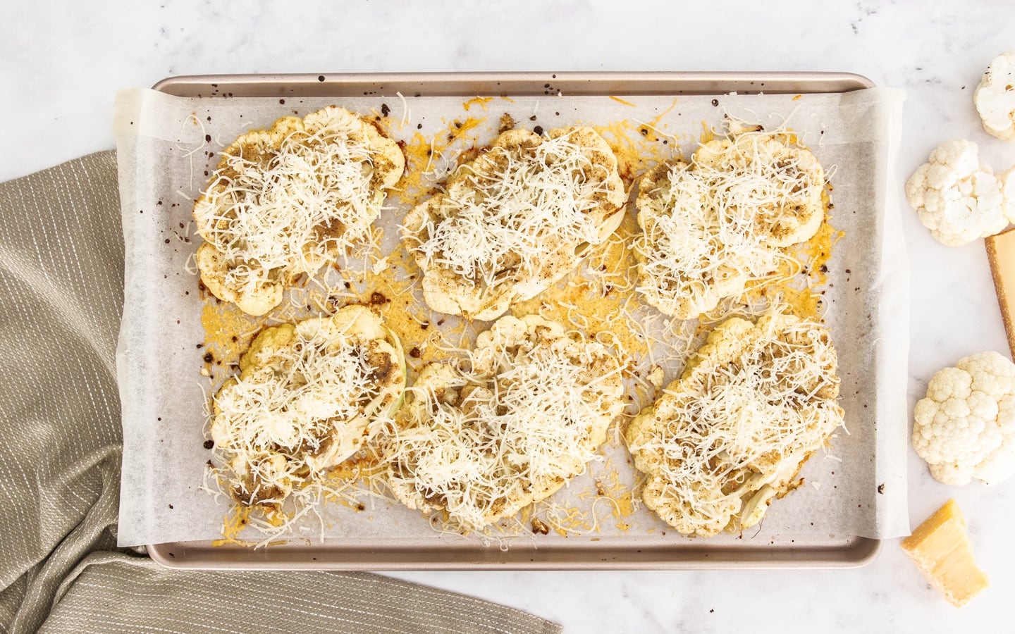Cauliflower steaks topped with chees on a baking sheet.