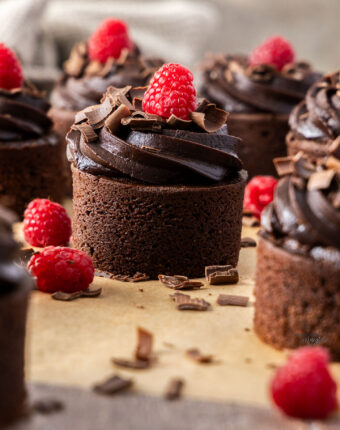 Closeup of a choc mini cake topped with chocolate shavings and a raspberry.