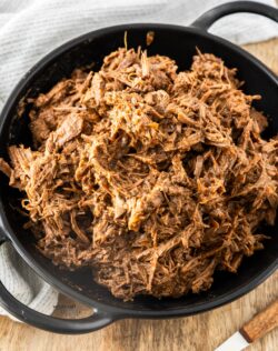 A batch of slow cooker pulled beef in a black bowl.