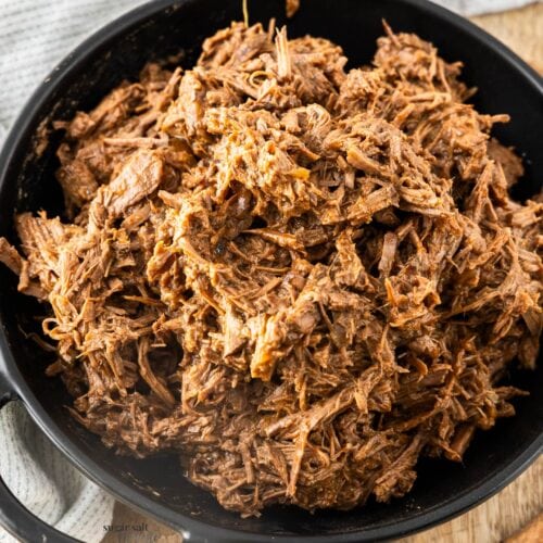 A batch of slow cooker pulled beef in a black bowl.