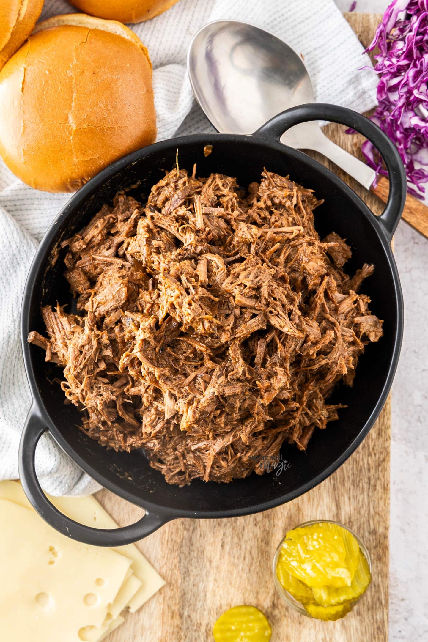 Top down view of pulled beef in a bowl with burger fixing around it.