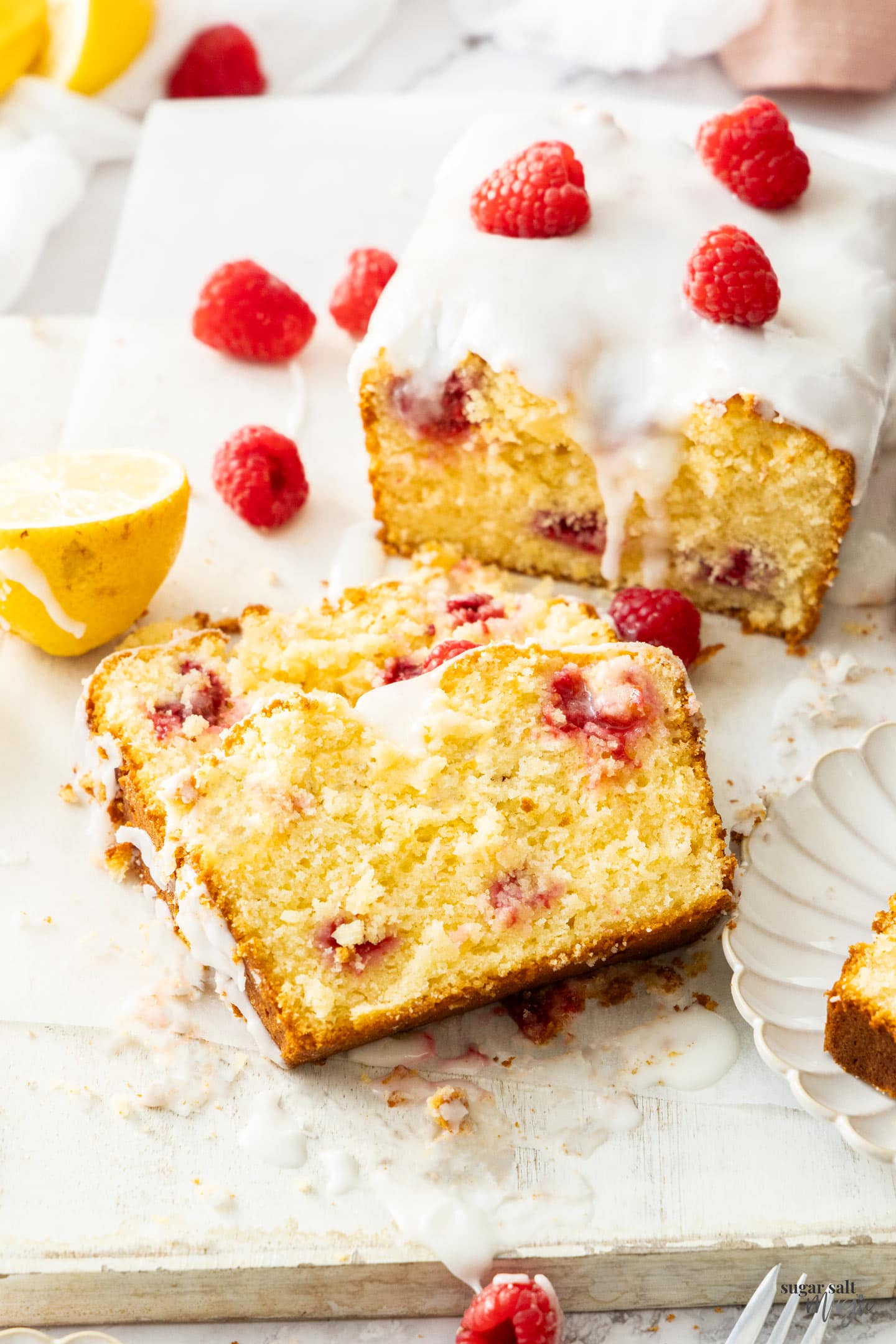 Two slices of lemon raspberry loaf cake stacked on a wooden board.