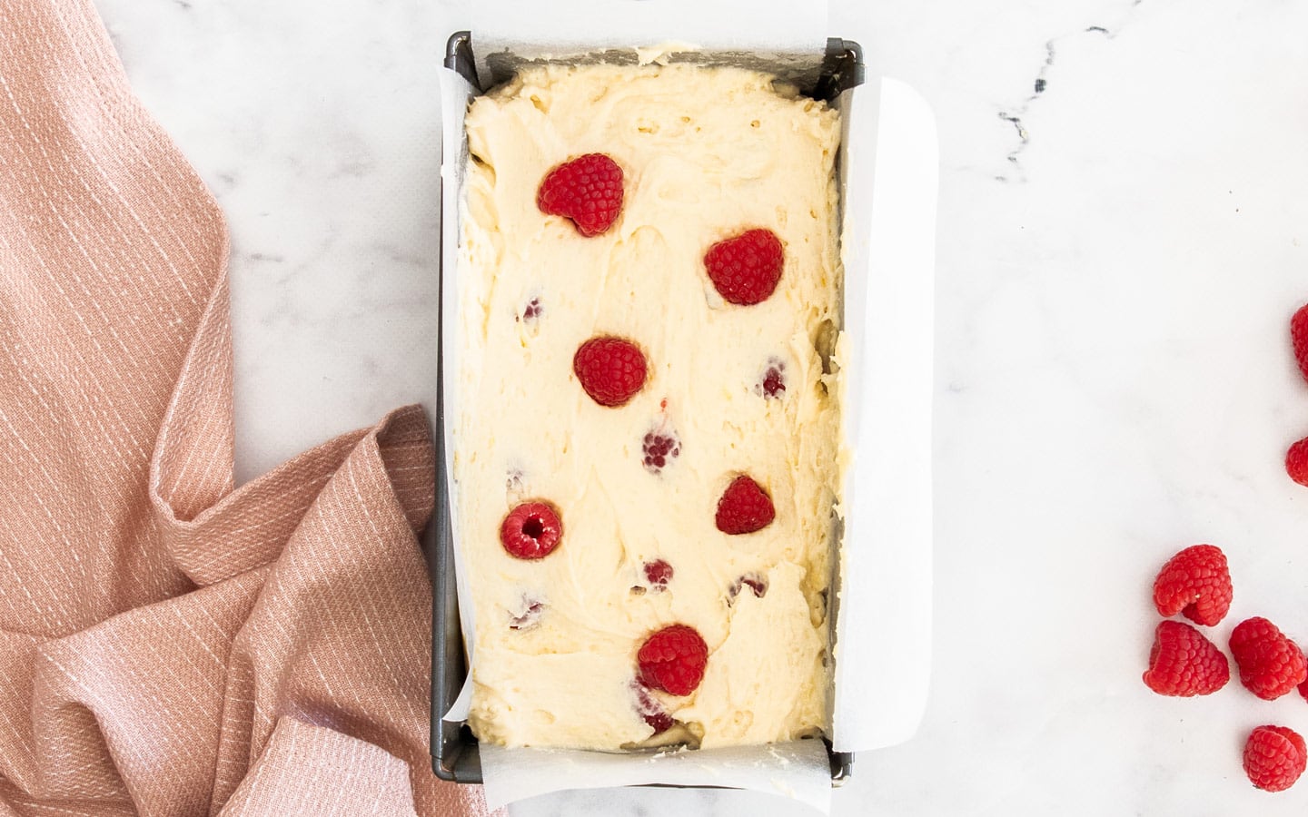 The batter in the loaf pan with some raspberries dotted on top.